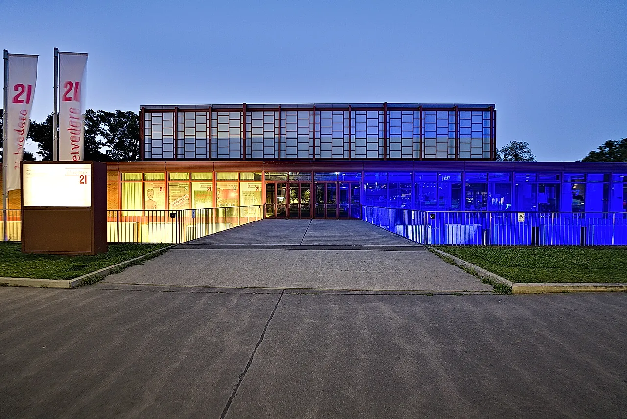 Belvedere 21 at dusk, its glass front lit up in blue